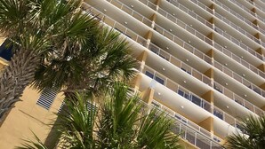 A high-rise building with multiple balconies, a central vertical corridor, and surrounding palm trees. - Beautiful 2/2 Condo at Sterling Reef~Great location~Sleeps 6~Beach svc. included (Panama City Beach)