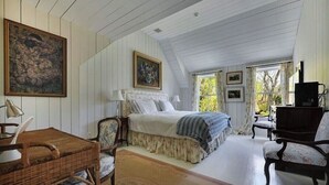 A cozy bedroom with a large bed, a desk, and a chair. There are framed pictures on the wall and a fireplace. - Southampton Home #6 (Southampton)