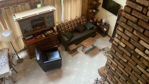 A cozy living room with a fireplace, a sofa, a coffee table, and a television. - Cozy rustic A-Frame close to Seven Springs and Hidden Valley (Champion)