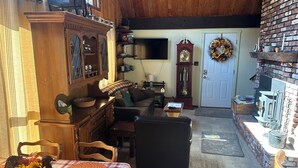 A cozy living room with a fireplace, wooden furniture, and a large clock. - Cozy rustic A-Frame close to Seven Springs and Hidden Valley (Champion)