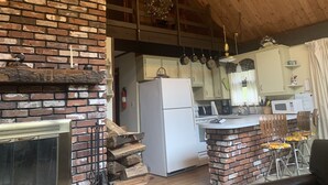 A rustic kitchen with a brick fireplace, a refrigerator, and wooden ceiling beams. - Cozy rustic A-Frame close to Seven Springs and Hidden Valley (Champion)