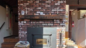 A brick fireplace with a wood stove, a clock, and a shelf with various items. - Cozy rustic A-Frame close to Seven Springs and Hidden Valley (Champion)