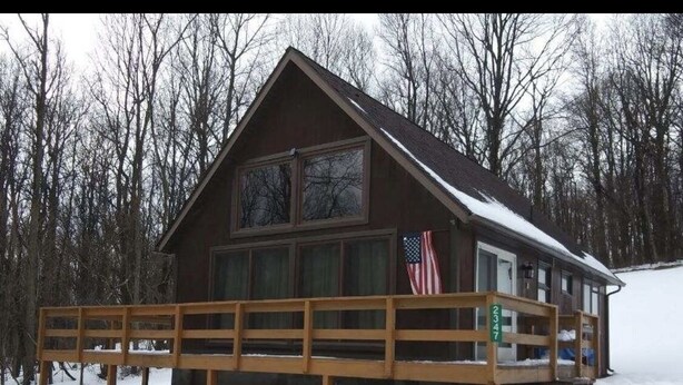 A cabin with a wooden deck, large windows, and an American flag. - Cozy rustic A-Frame close to Seven Springs and Hidden Valley (Champion)