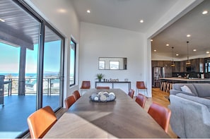 A modern dining room with a large wooden table, surrounded by chairs, and a view of the outdoors.