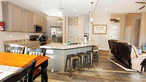 A modern kitchen with a central island, bar stools, and a dining table.