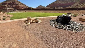 A landscaped outdoor area with a grassy lawn, a rock feature, and a building in the background. - Maison Sans Souci - Kanab Home, Pool & Views (Kanab)