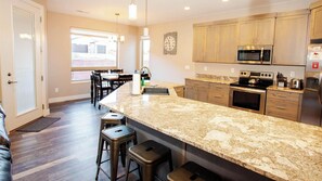 A kitchen with granite countertops, stainless steel appliances, wooden cabinets, and a dining area with a table and chairs.