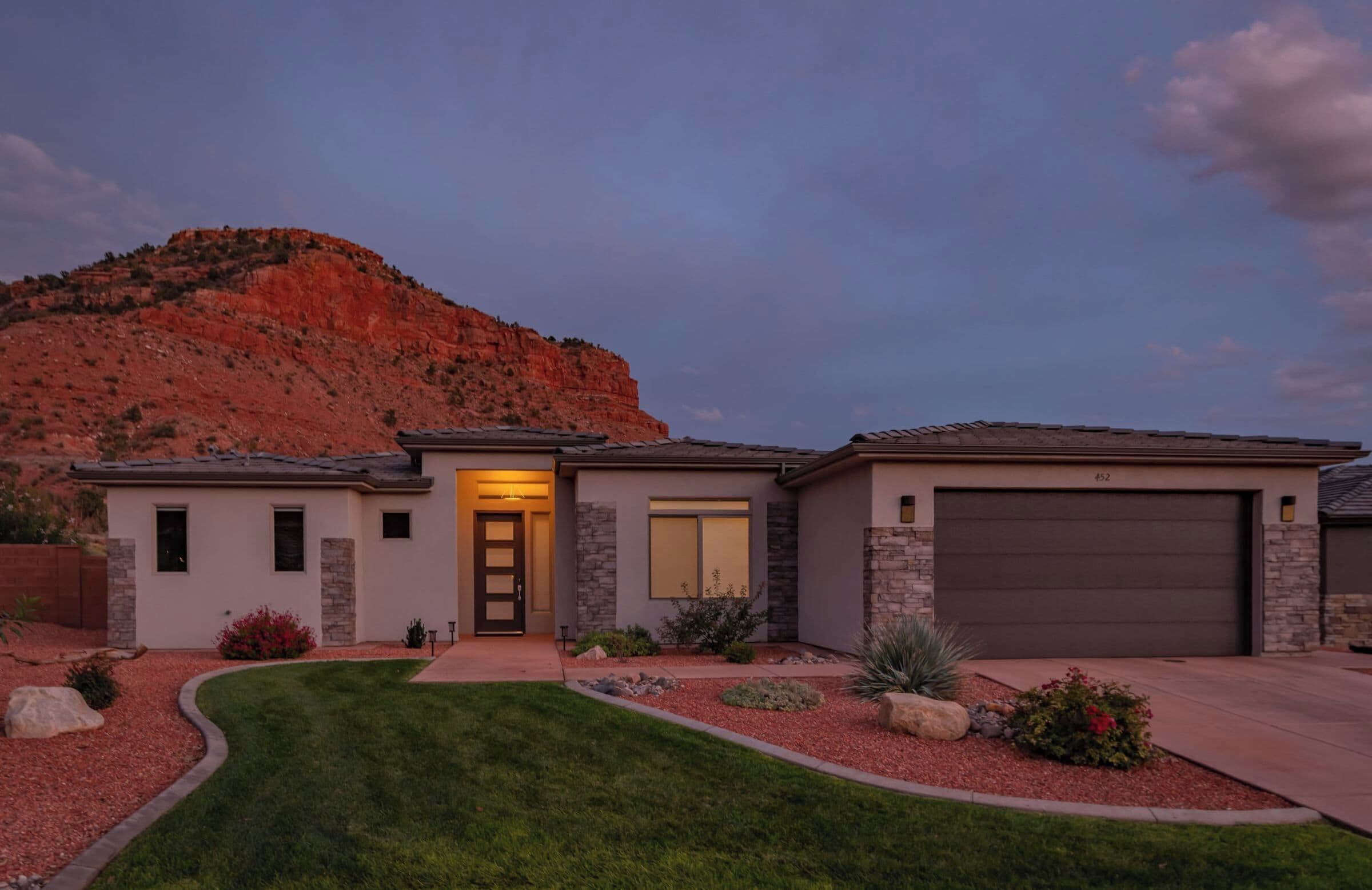 A modern two-story house with a stone facade, a garage, and a well-maintained lawn.