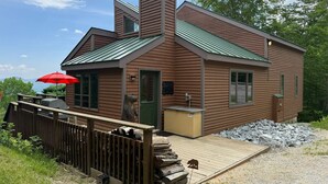 Une cabane avec un toit végétalisé, une cheminée et une terrasse en bois.