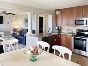 A modern kitchen with stainless steel appliances, wooden cabinets, and a dining area with white chairs and a glass table. - Beachfront Hilton Head Resort 2BR (AR-412): Tennis, Pickleball & Largest Pool (Hilton Head Island)