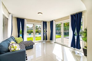 A modern living room with a sofa, patterned cushions, and large windows with curtains.