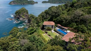 A coastal property with a swimming pool, surrounded by lush greenery and rocky terrain.