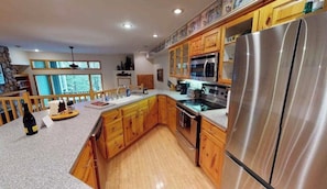 A kitchen with wooden cabinets, a stainless steel refrigerator, and a large island with a sink.