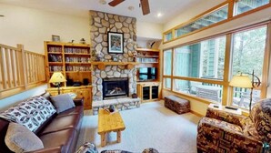 Una sala de estar acogedora con una chimenea de piedra, estanterías, un sofá y ventanas grandes.