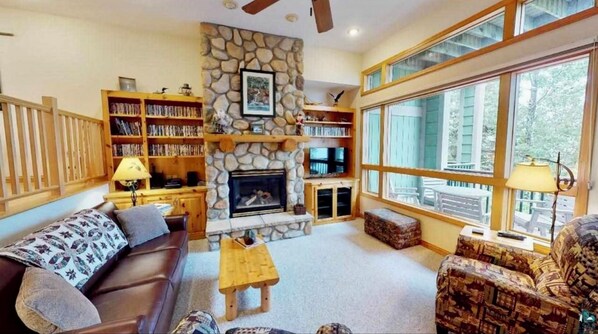 Relax in the living room with a fireplace, bookshelves, and comfortable seating, offering a view of the outdoors.