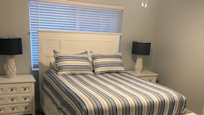 A bedroom with a bed, two bedside tables, a ceiling fan, and a window with blinds. - Sunsets at Gulf of Mexico (Venice)