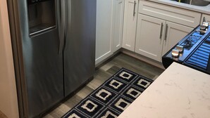 A modern kitchen with stainless steel appliances, white cabinetry, a patterned backsplash, and a window with blinds. - Sunsets at Gulf of Mexico (Venice)
