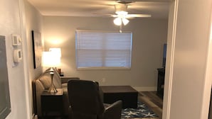 A room with a ceiling fan, a window with blinds, a desk with a lamp, a chair, and a small rug on the floor. - Sunsets at Gulf of Mexico (Venice)
