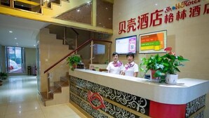A hotel reception desk with two staff members, a staircase, and a wall with a sign in a foreign language. - Shell Hefei Chaohu Railway Station Wanda Plaza Hotel (Hefei)