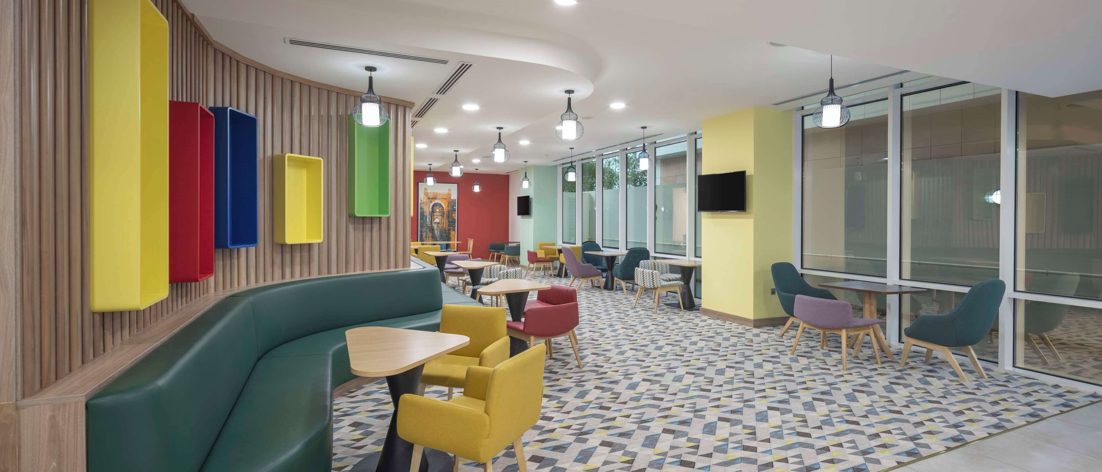 Un espace intérieur moderne avec un canapé vert aux lignes courbes, des chaises jaunes et rouges, et un sol à motifs.