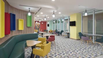 A modern indoor space with a curved green sofa, yellow and red chairs, and a patterned floor.