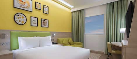 Habitación de hotel con una cama grande, un cabecero verde, una pared de acento amarilla y obras de arte.