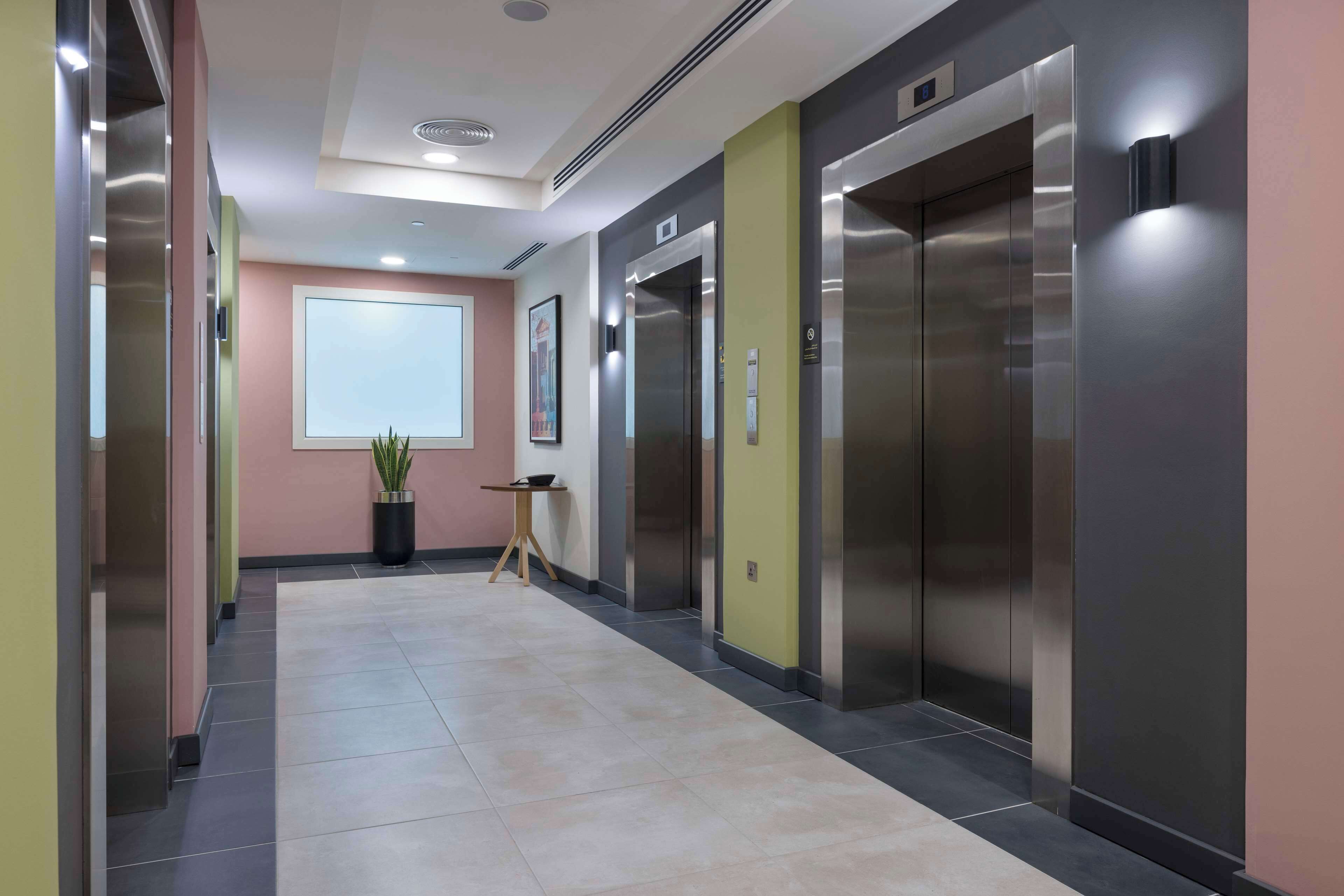 A modern elevator area with stainless steel elevators, a potted plant, and a small table.