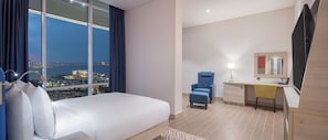 A hotel room with a bed, a desk, a chair, a mirror, and a view of a cityscape. - Hampton by Hilton Doha Old Town (Doha)