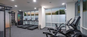 A modern gym with treadmills, weight machines, and a large window offering a view of the outdoors. - Hampton by Hilton Doha Old Town (Doha)