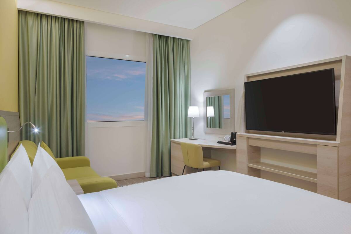 A hotel room with a bed, a desk, a chair, a television, and a window with curtains.