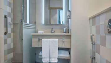 Un baño moderno con cabina de ducha de vidrio, tocador de madera con espejo y lavamanos blanco.