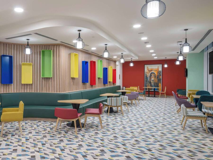 Un interior moderno con un sofá verde, sillas amarillas y rojas, y un suelo estampado.