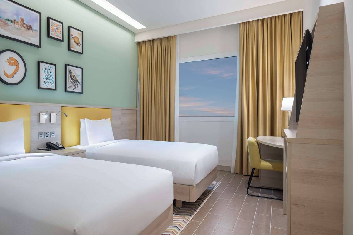 A hotel room with two beds, a desk, a chair, and a TV.