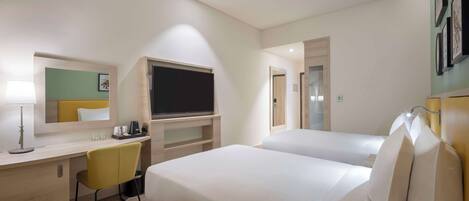 Habitación de hotel con dos camas, un escritorio con silla, un televisor de pantalla plana, un espejo y una pequeña zona de café.