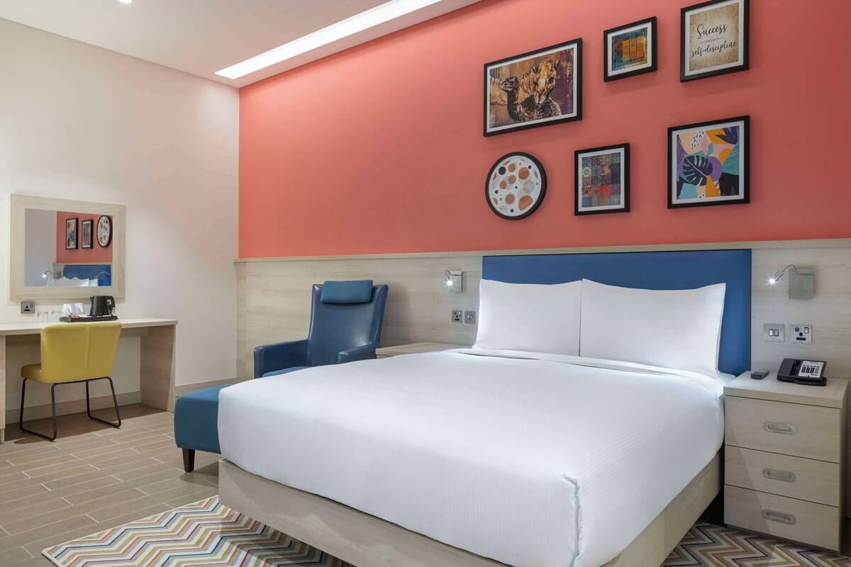 A hotel room with a bed, a desk, and a chair. There are framed pictures on the wall.