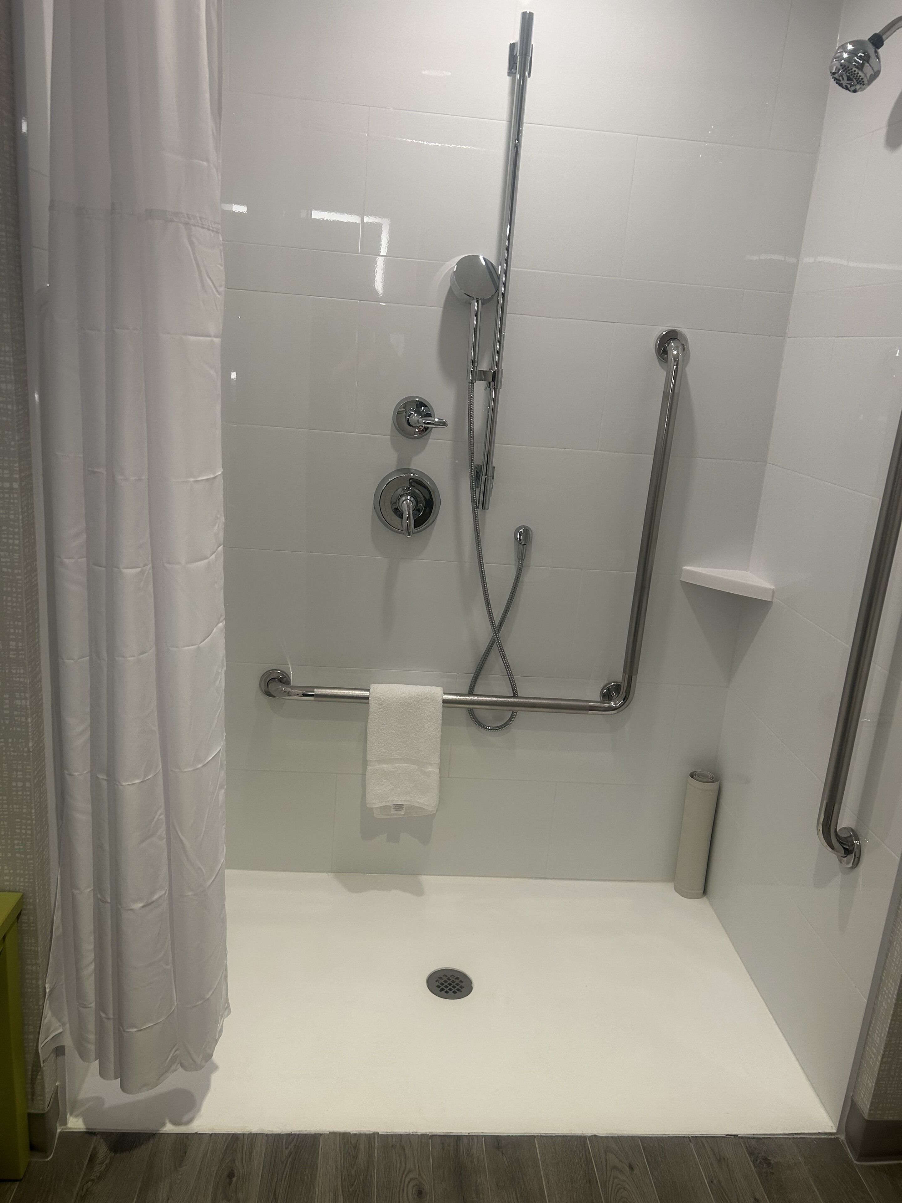 Eine ebenerdige Dusche mit Haltegriff, Handtuchhalter und Duschkopf.
