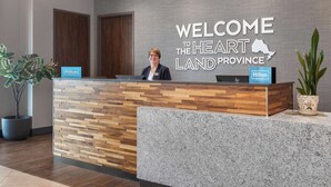 A reception desk with a "Welcome to the Heartland Province" sign, a Hilton Honors logo, and a potted plant. - Hampton Inn by Hilton Kingston (Kingston)