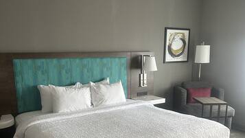 A hotel room with a large bed, a nightstand, a chair, and a wall-mounted lamp.