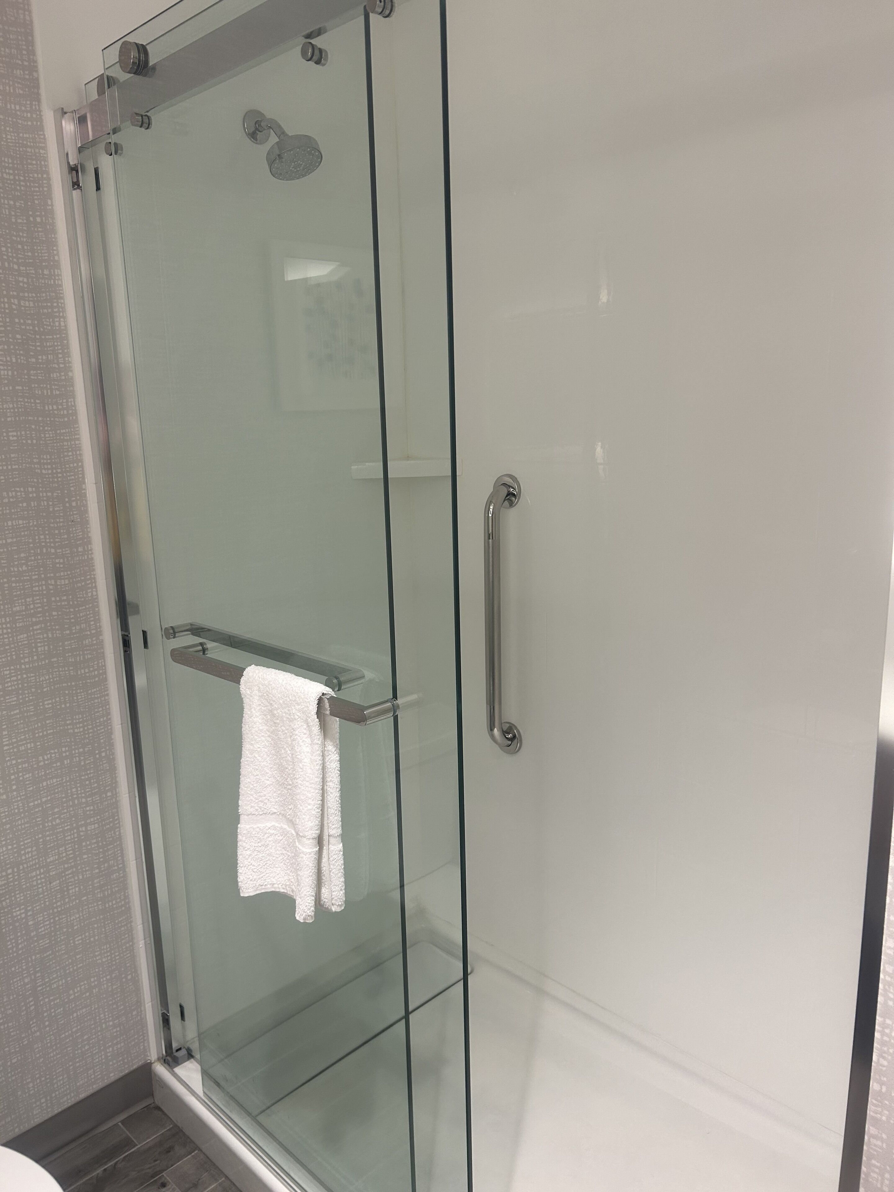 Ducha con cerramiento de vidrio, barra para toallas y pasamanos.