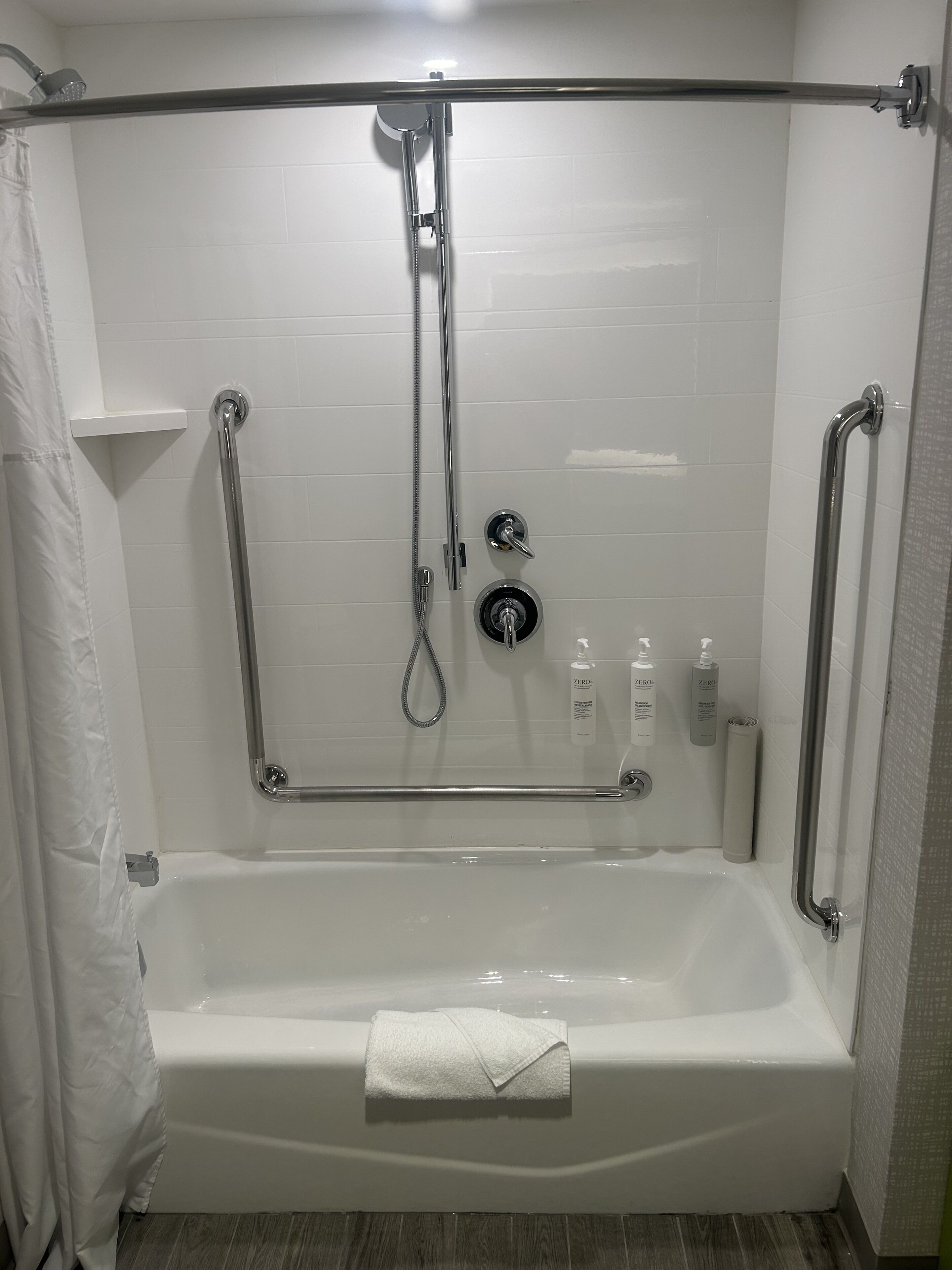 A walk-in shower with a bathtub, grab bars, and a handheld showerhead.