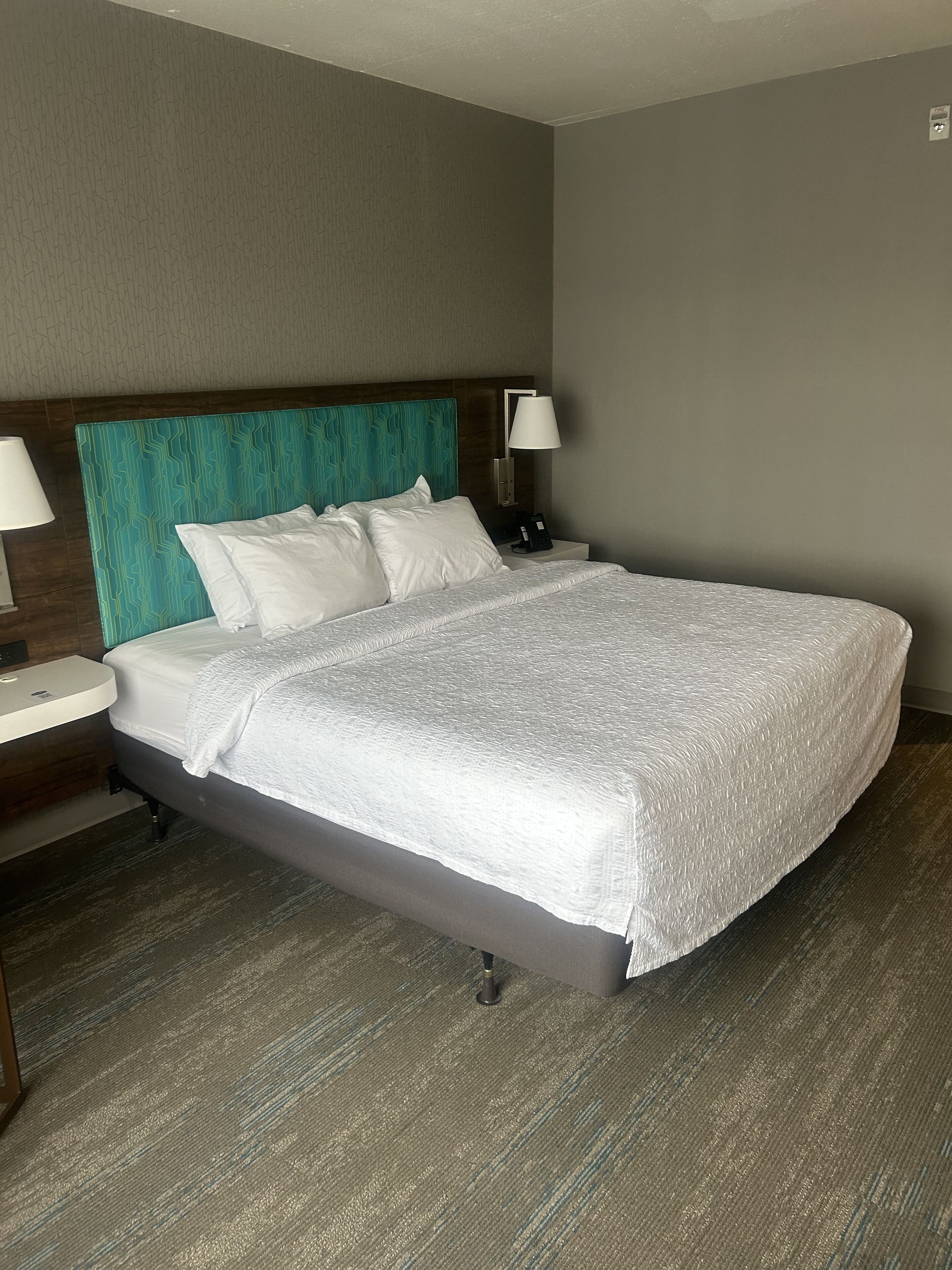 A hotel room with a bed, two bedside tables, a nightstand, and a wall-mounted lamp.