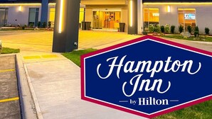 A Hampton Inn by Hilton hotel with a modern design, featuring a prominent red logo, a covered entrance, and a well-lit facade. - Hampton Inn by Hilton Kingston (Kingston)