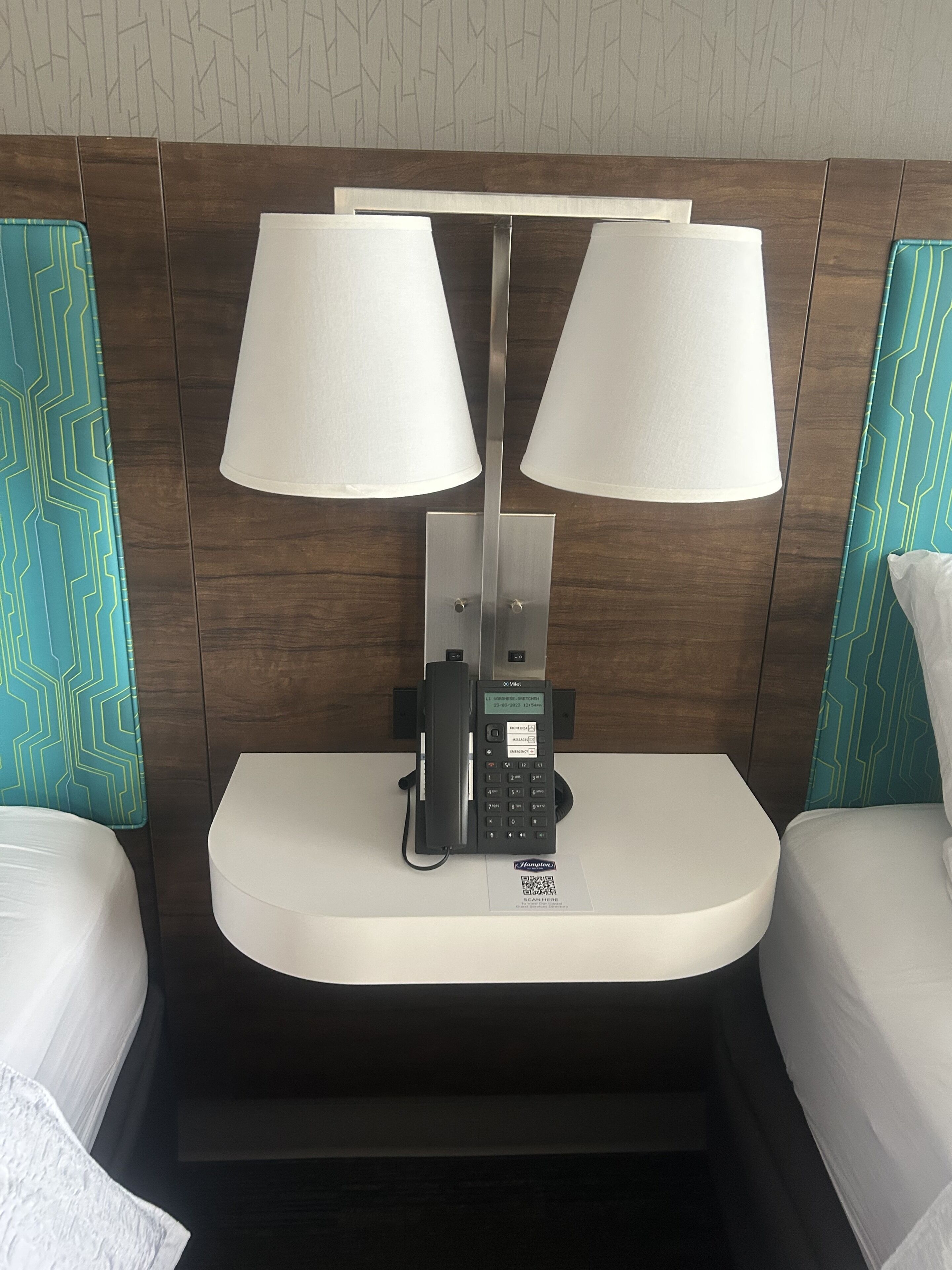 A hotel room with a bedside table featuring a telephone and a lamp.