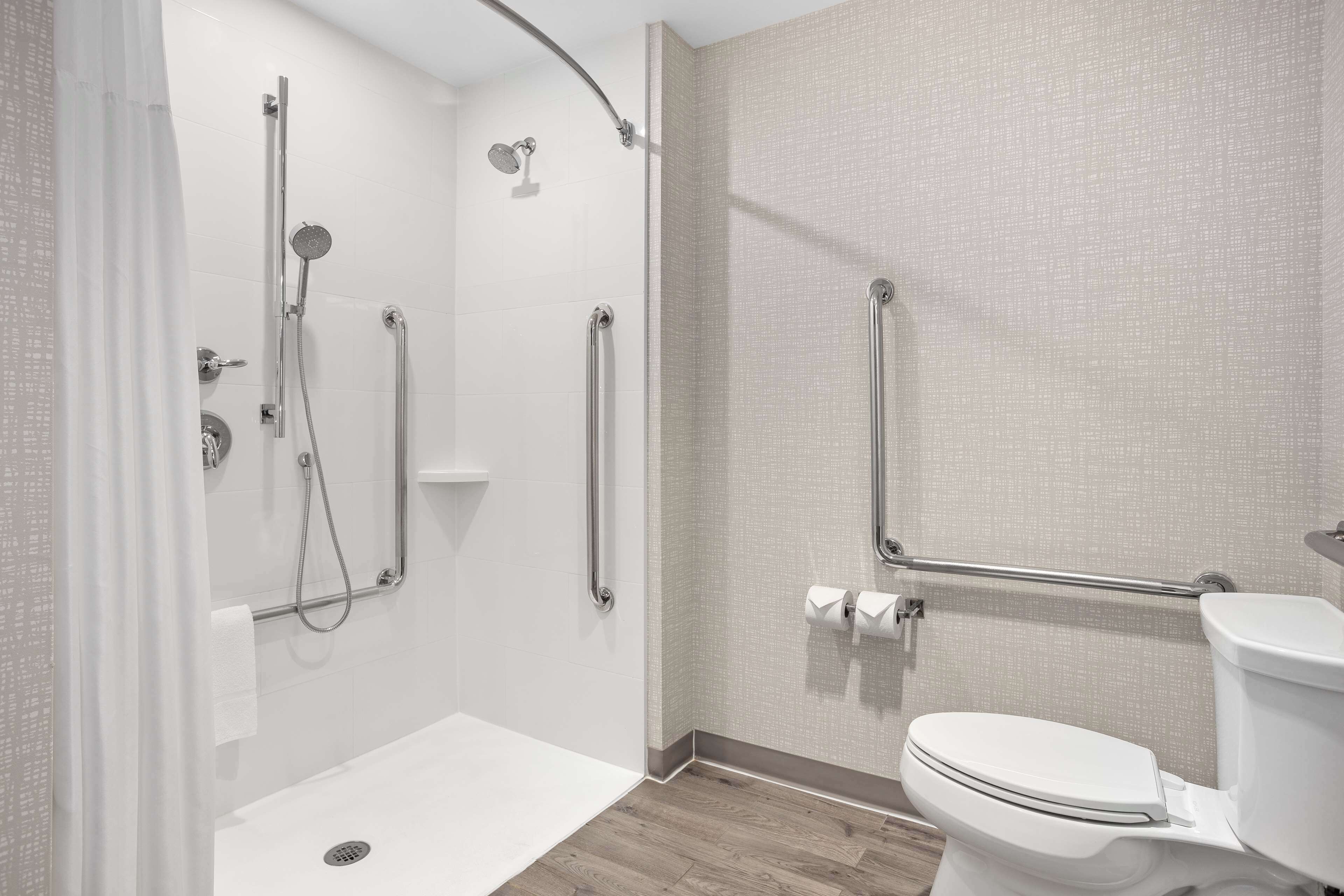 A modern bathroom with a walk-in shower, grab bars, a toilet, and a white sink.