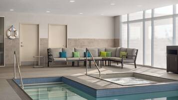 A modern indoor pool area with a seating area, a hot tub, and a view through large windows.
