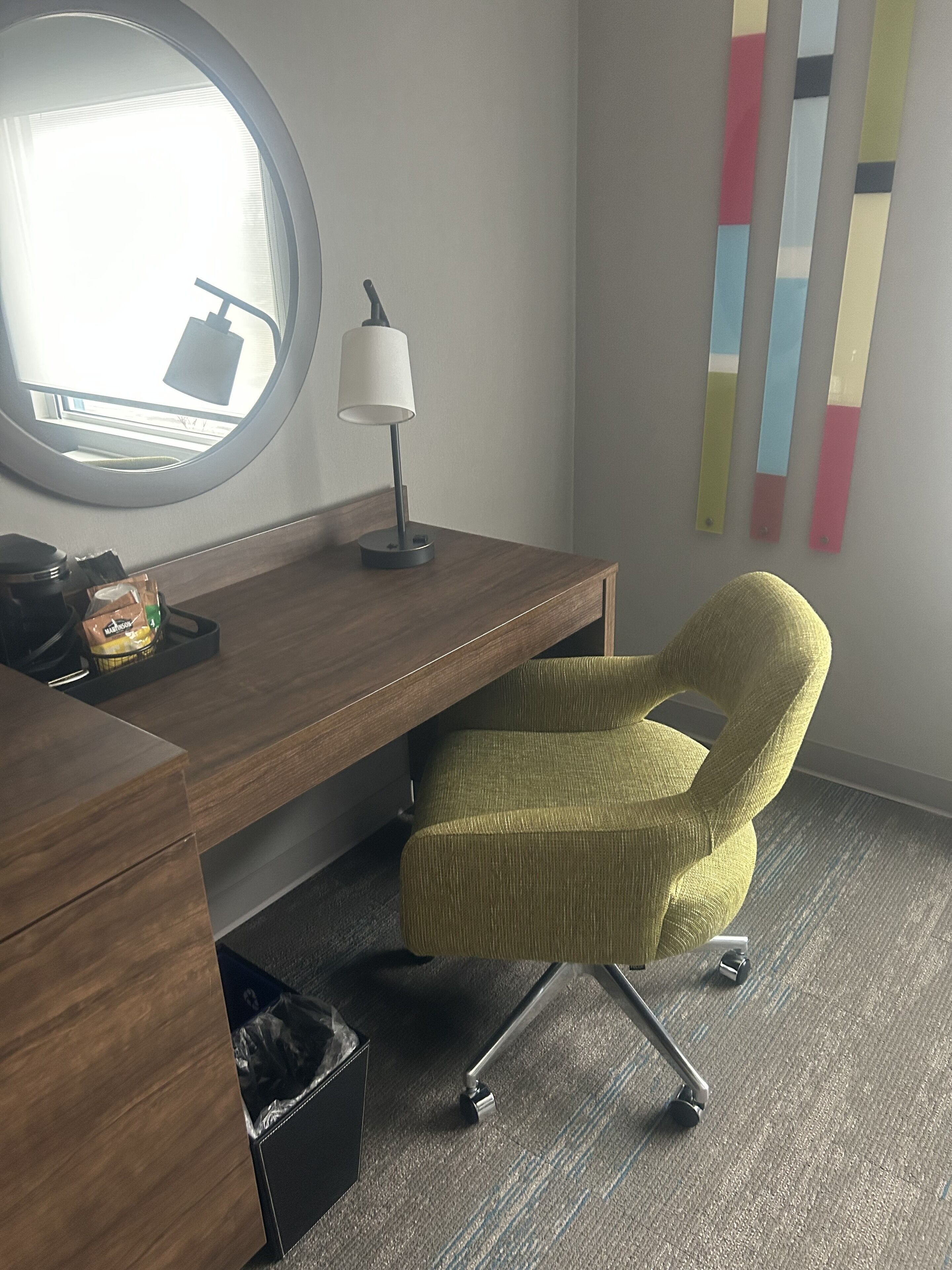 Un bureau moderne avec une lampe, une chaise de bureau verte et une poubelle.