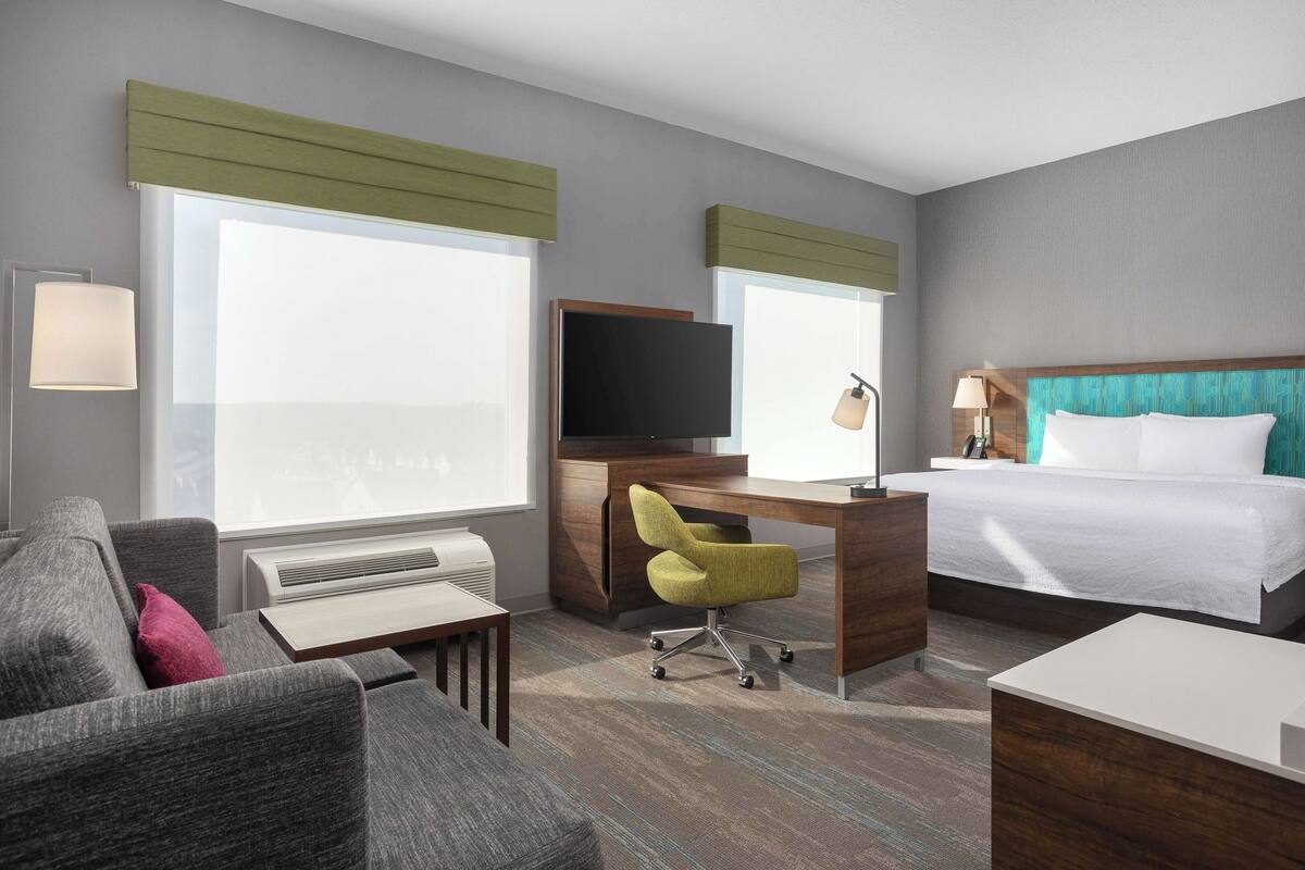 Una habitación de hotel con una cama grande, un escritorio con una silla, un televisor y un sofá.