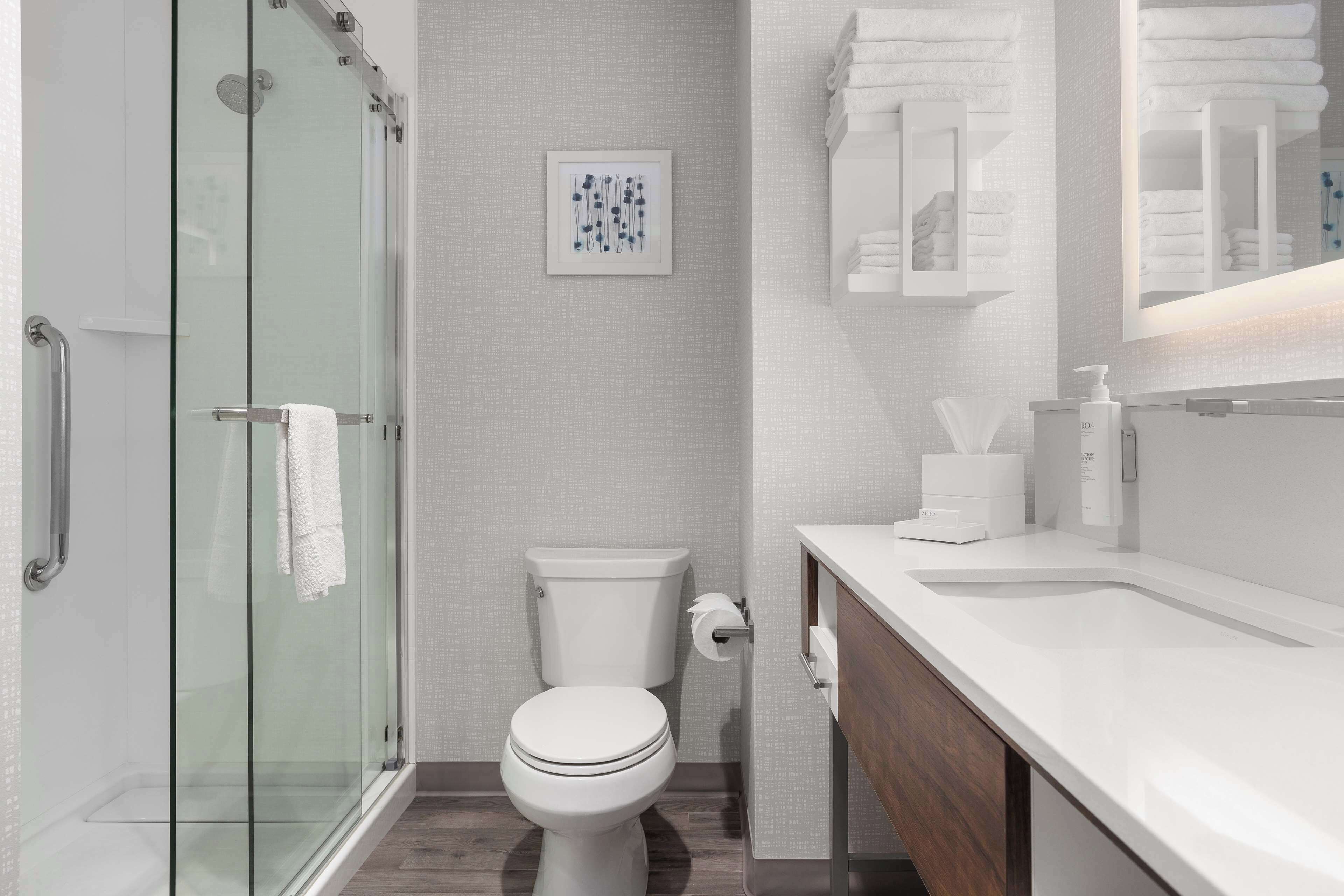 A modern bathroom with a glass shower enclosure, a toilet, a sink with a mirror, and neatly arranged towels.