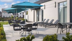 An outdoor patio area with tables and chairs, a large umbrella, and a poolside lounge area. - Hampton Inn by Hilton Kingston (Kingston)