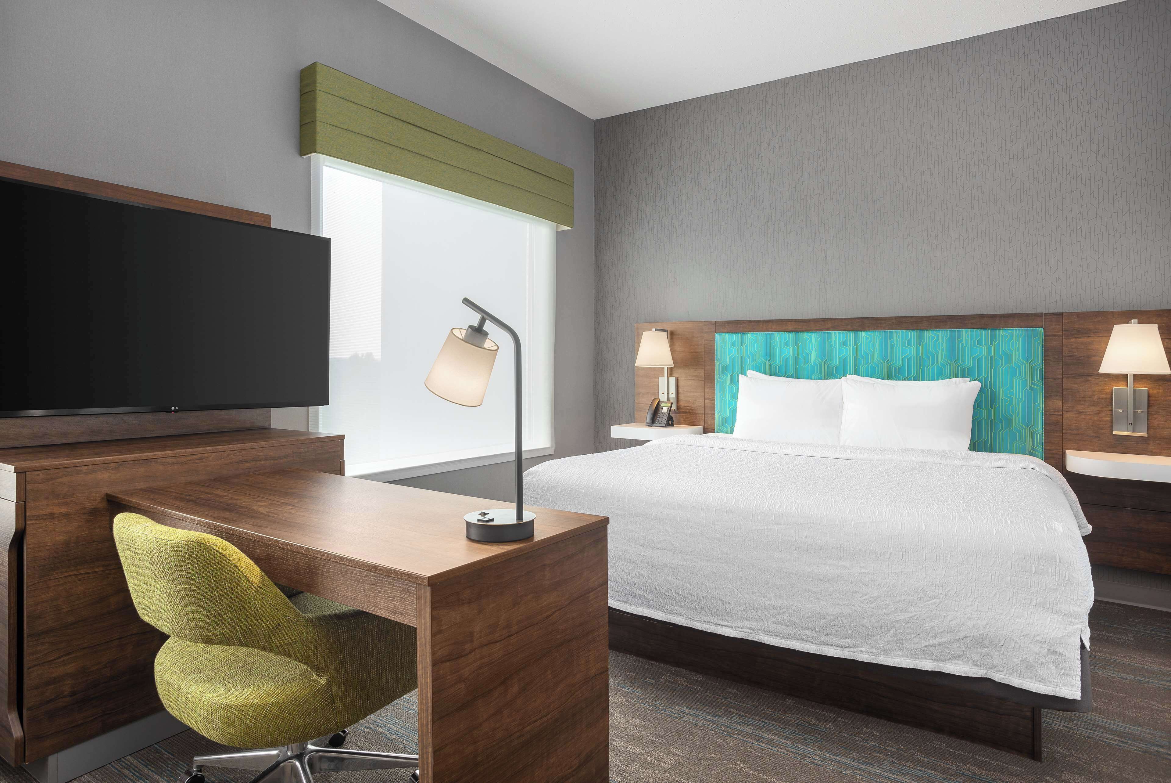 A hotel room with a bed, a desk with a chair, a TV, and two bedside lamps.